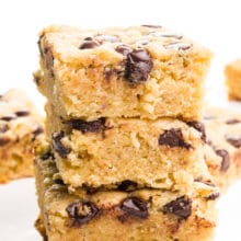 A closeup of a stack of vegan blondie bars, showing chocolate chips on top and on the sides. There are more blondie slices in the background.