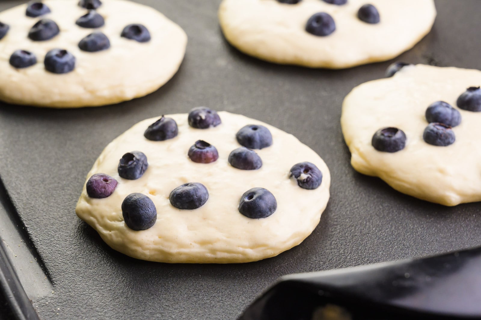 Blueberry pancakes are cooking on a griddle.