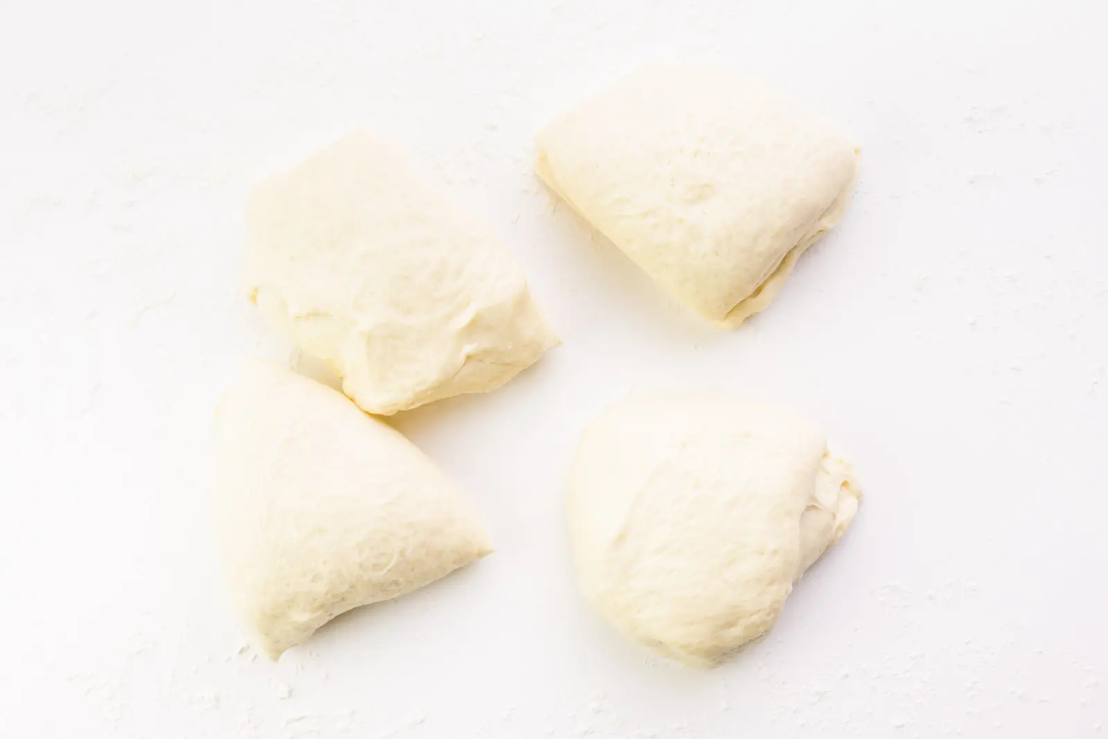 Dough has been cut into four equally-size pieces. These pieces are on a white counter.