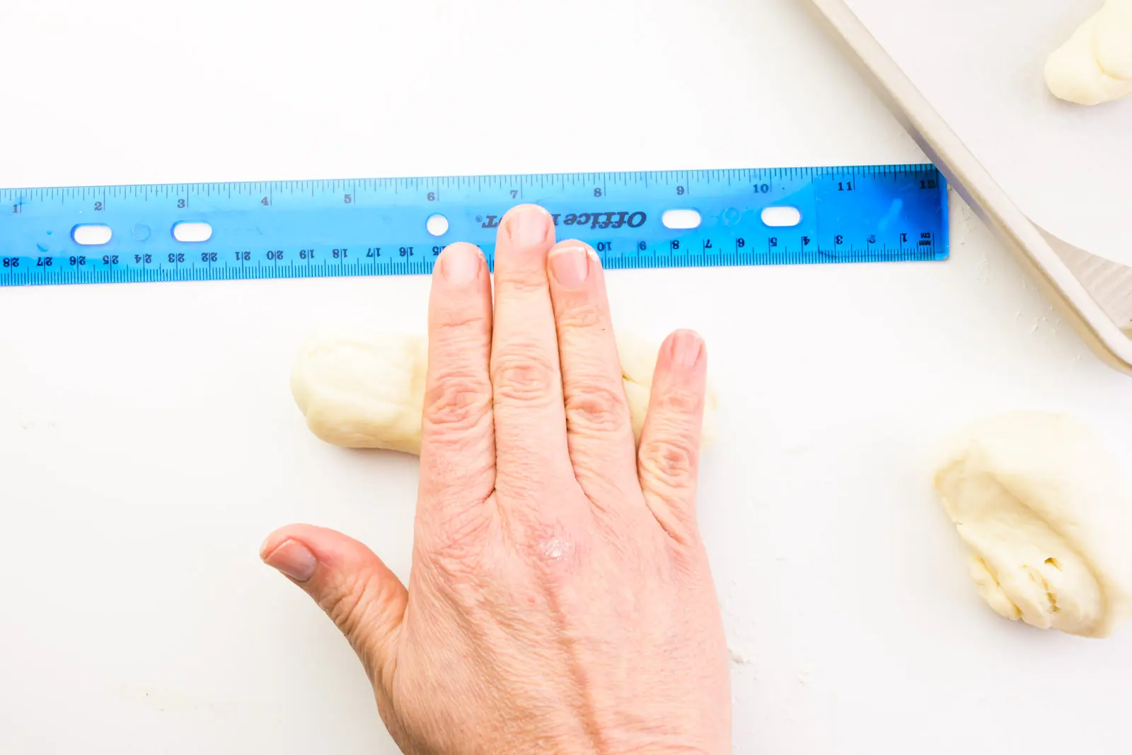 A hand is rolling a piece of dough next to a ruler. There are more dough pieces nearby.