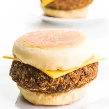 Vegan breakfast sausage patties are sandwiched between English muffins with cheese on top.