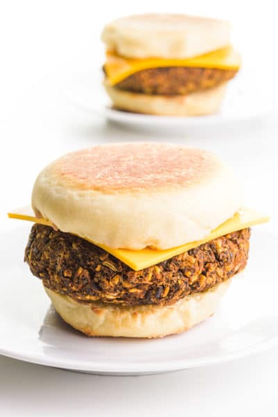 Vegan breakfast sausage patties are sandwiched between English muffins with cheese on top.