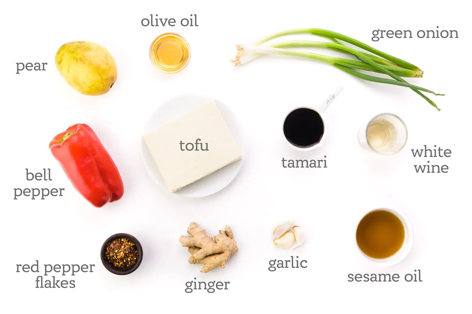 Ingredients are on a white counter. The labels next to them reads, "green onions, white wine, Tamari, sesame oil, garlic, ginger, red pepper flakes, bell pepper, tofu, pear, and olive oil."