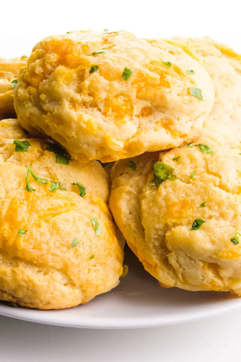 A plate holds several biscuits, showing cheese and flecks of chopped parsley on top.