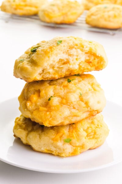 A stack of vegan cheddar bay biscuits shows the top one with a bite taken out. There are more biscuits in the background.