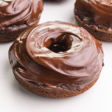 A closeup of a frosted chocolate donut. There are three donuts in the background.
