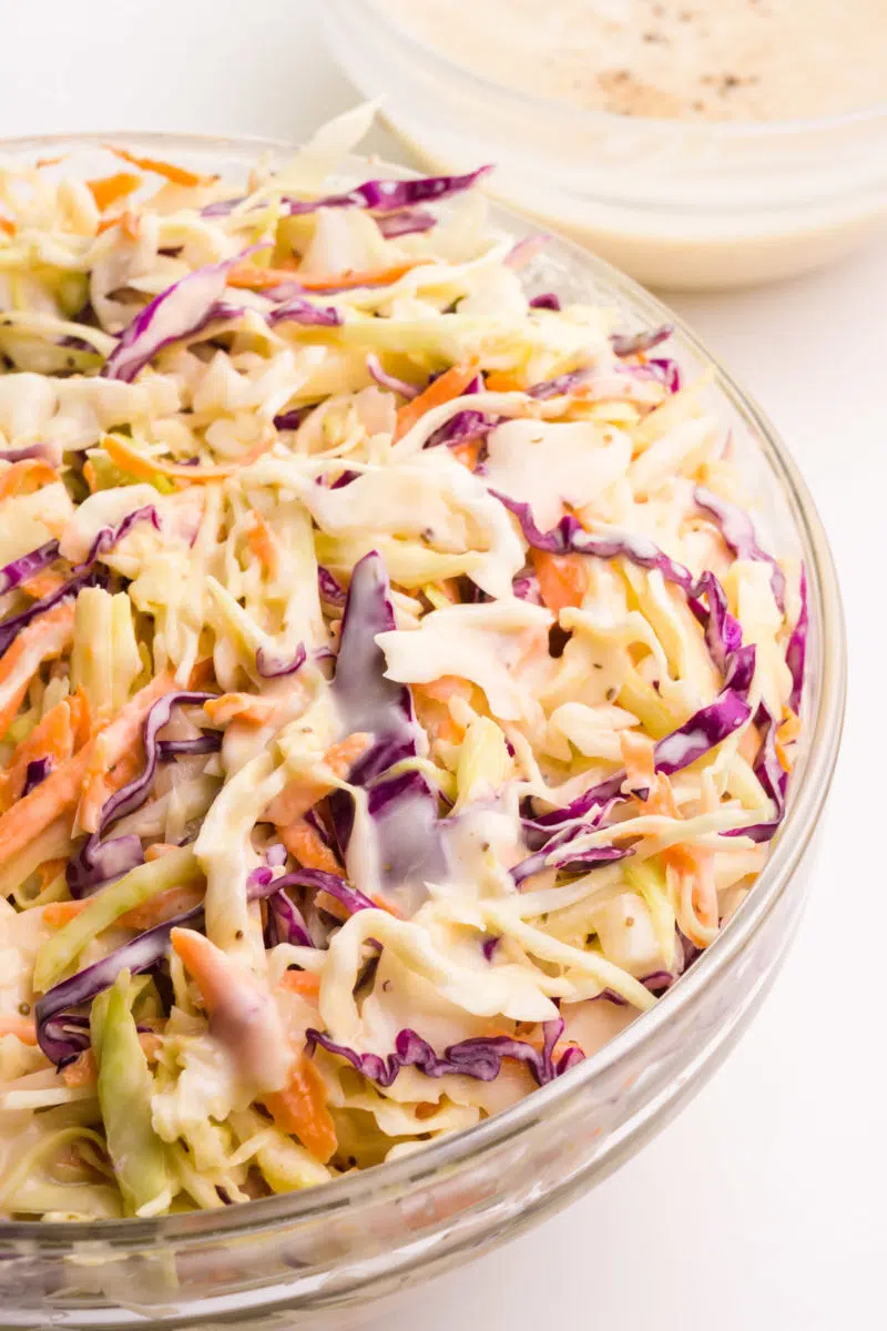 Looking down on the right side of a bowl of coleslaw with a bowl of more coleslaw sauce in the background.