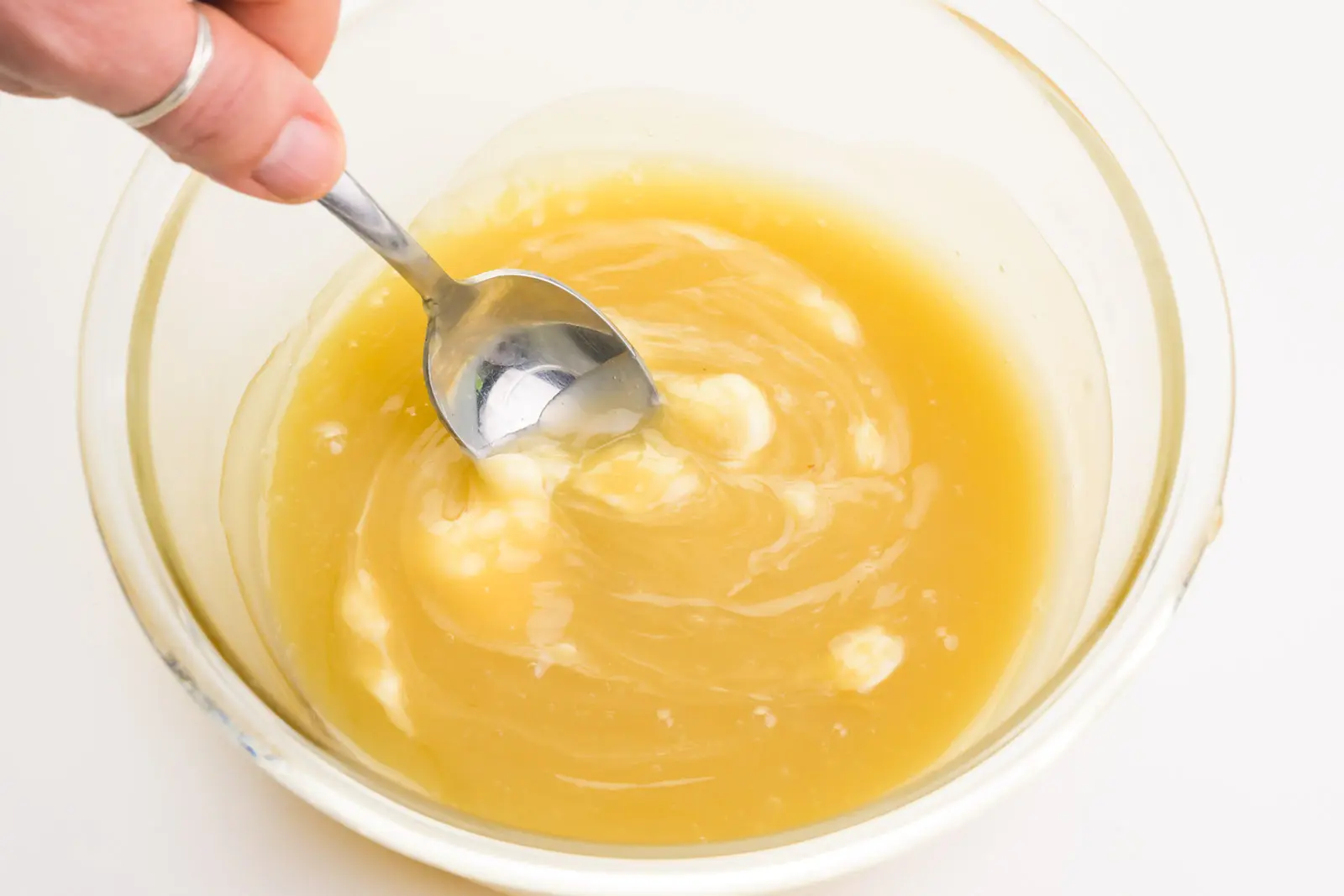 A hand holds a spoon, stirring vegan butter into a creamy mixture.