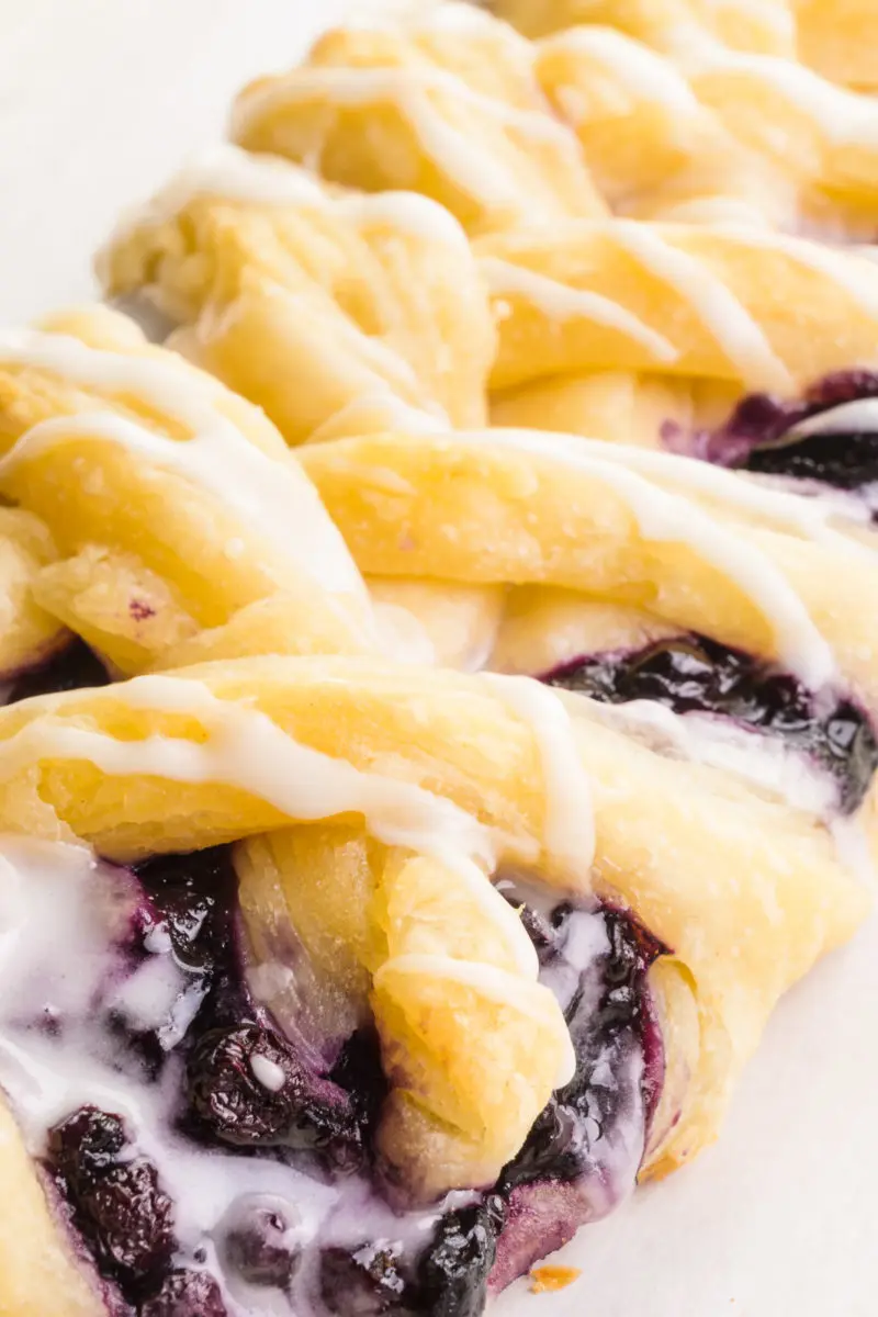 A close-up of a braided danish shows the blueberry filling, golden crust of the pastry, and vanilla glaze that's been drizzled over the top.