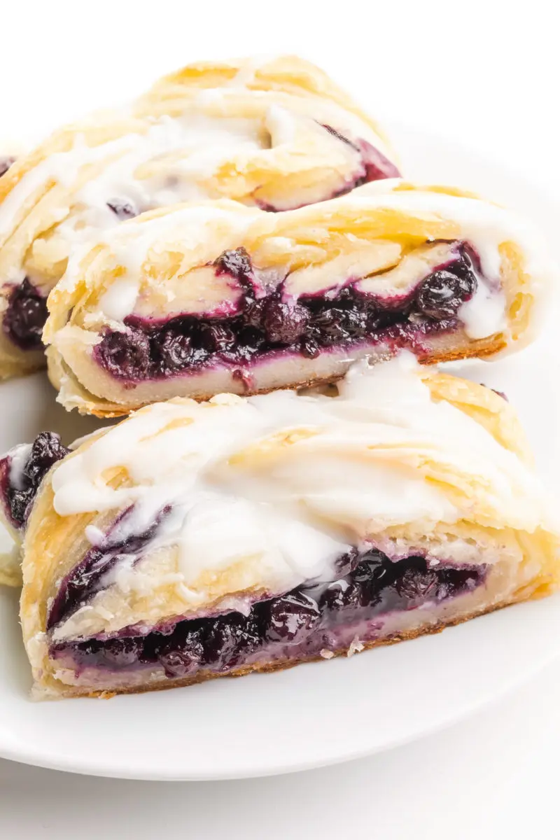 A vegan danish sits on a plate. It has blueberry filling and vanilla glaze on top.