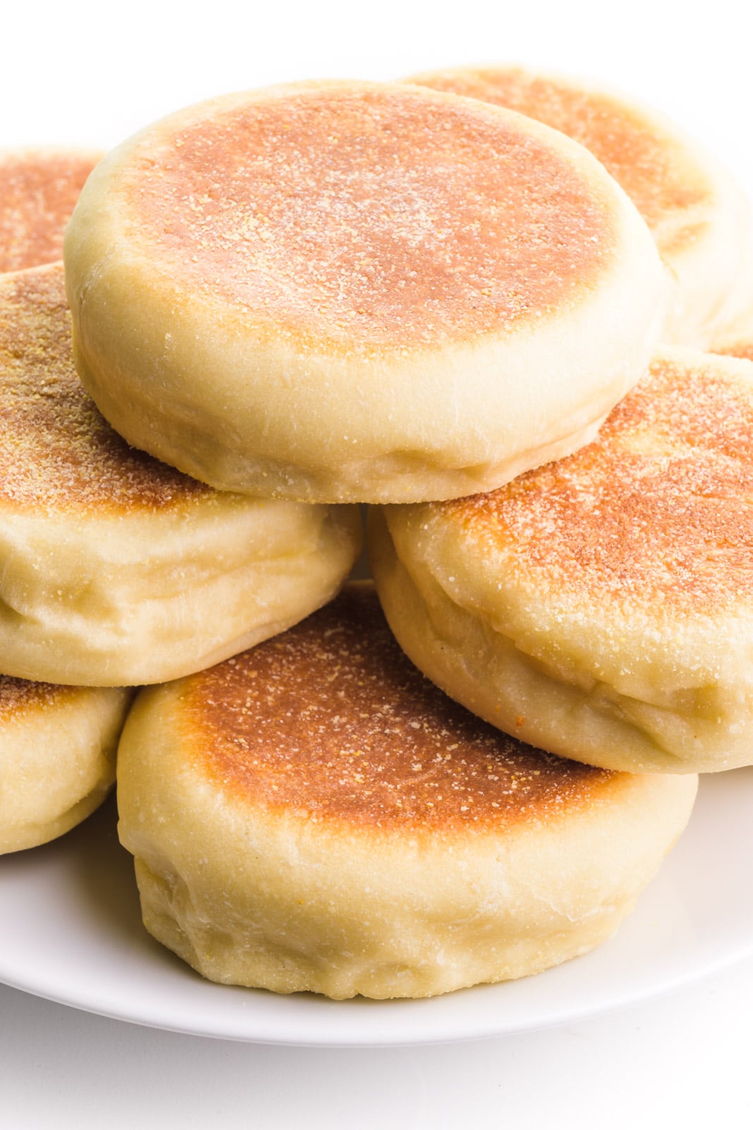 Several English muffins sit on a plate, showing golden-brown crusts on top.