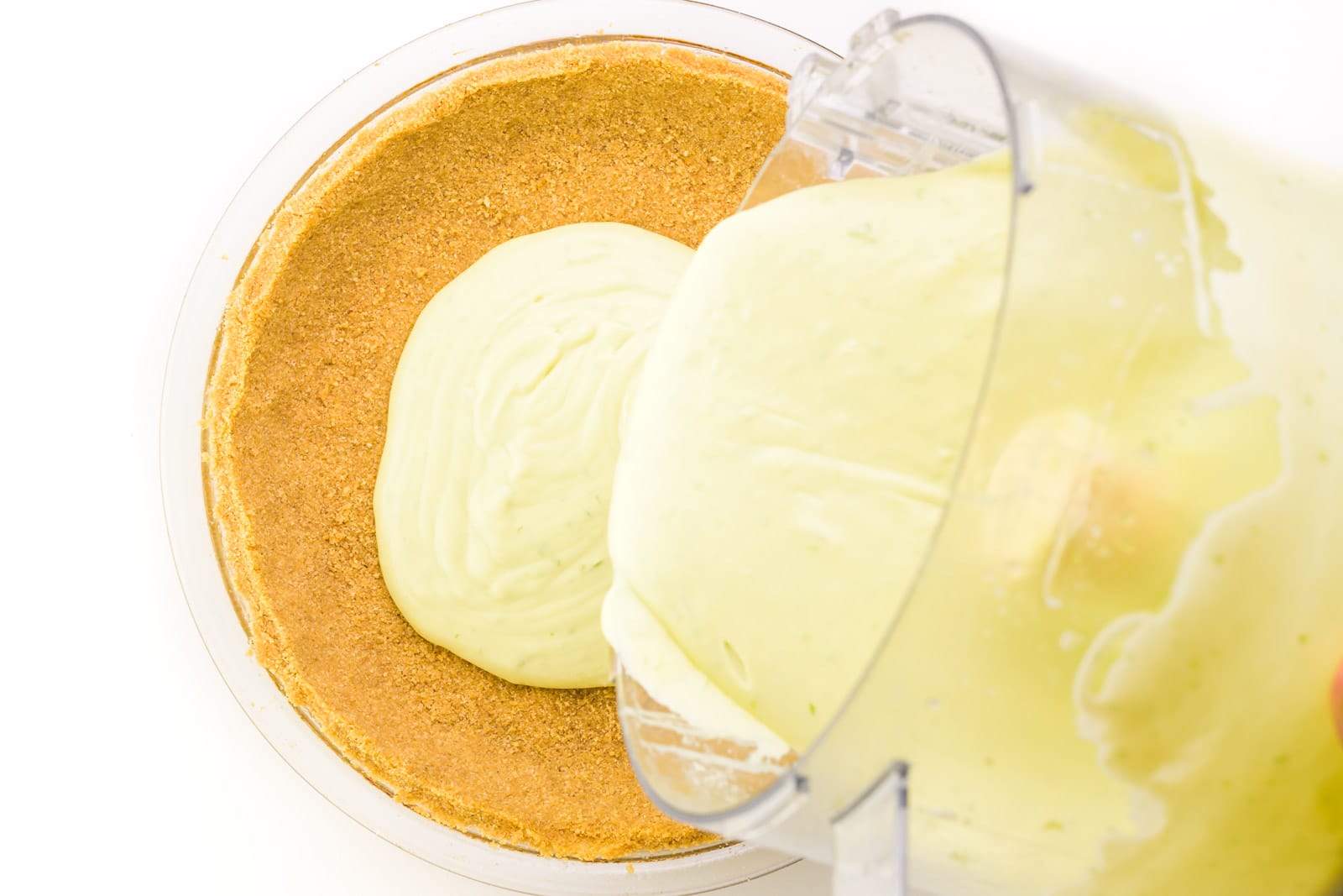Key lime filling is being poured into a graham cracker crust.