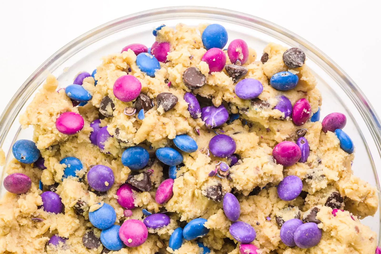 Looking down on a glass bowl full of cookie dough with chocolate chips and colorful candy pieces.