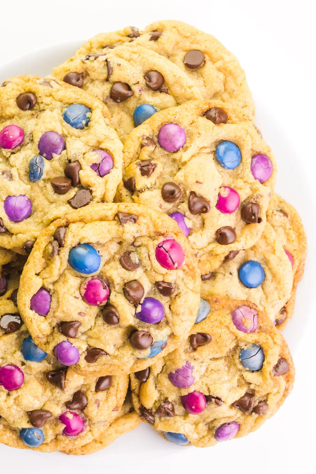 Looking down on a plate full of vegan M&M cookies, with each cookie full of chocolate chips and colorful candy pieces.