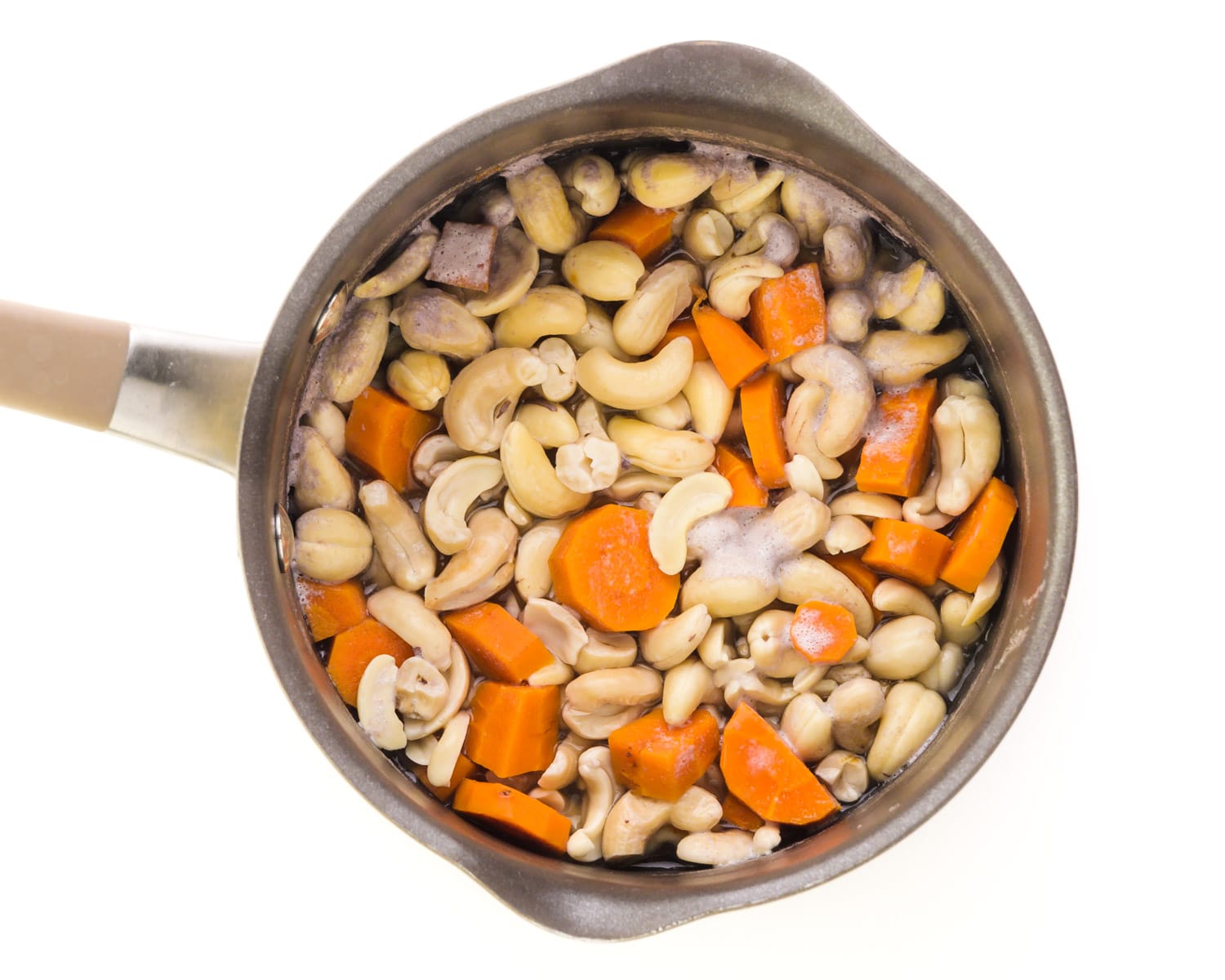 Looking down on a saucepan full of cooked cashews and sliced carrots.