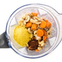 Looking down on a blender jar with ingredients like carrots, cashews, nutritional yeast flakes, chili powder, and more.