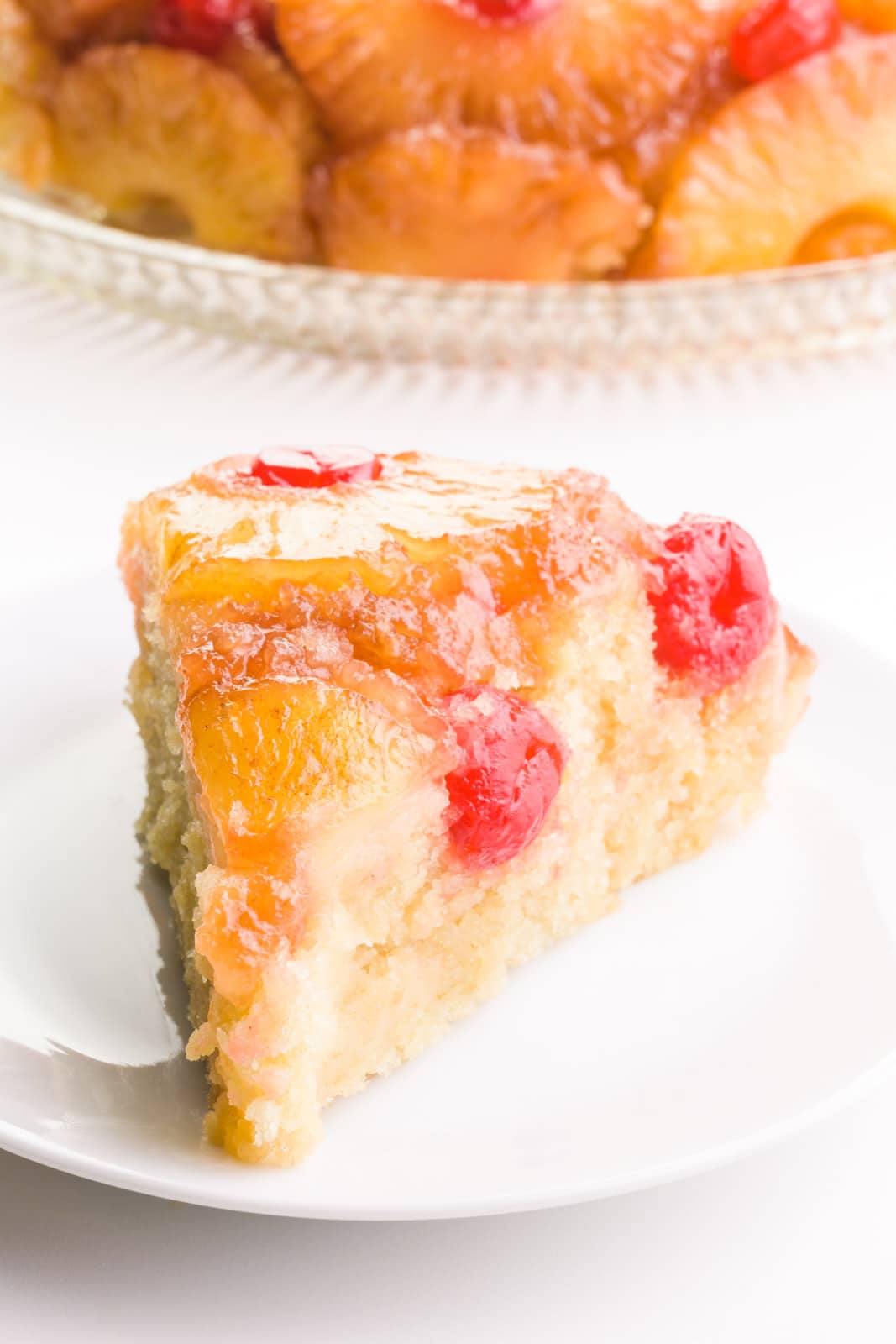 A slice of vegan pineapple upside down cake sits in front of the rest of the cake.