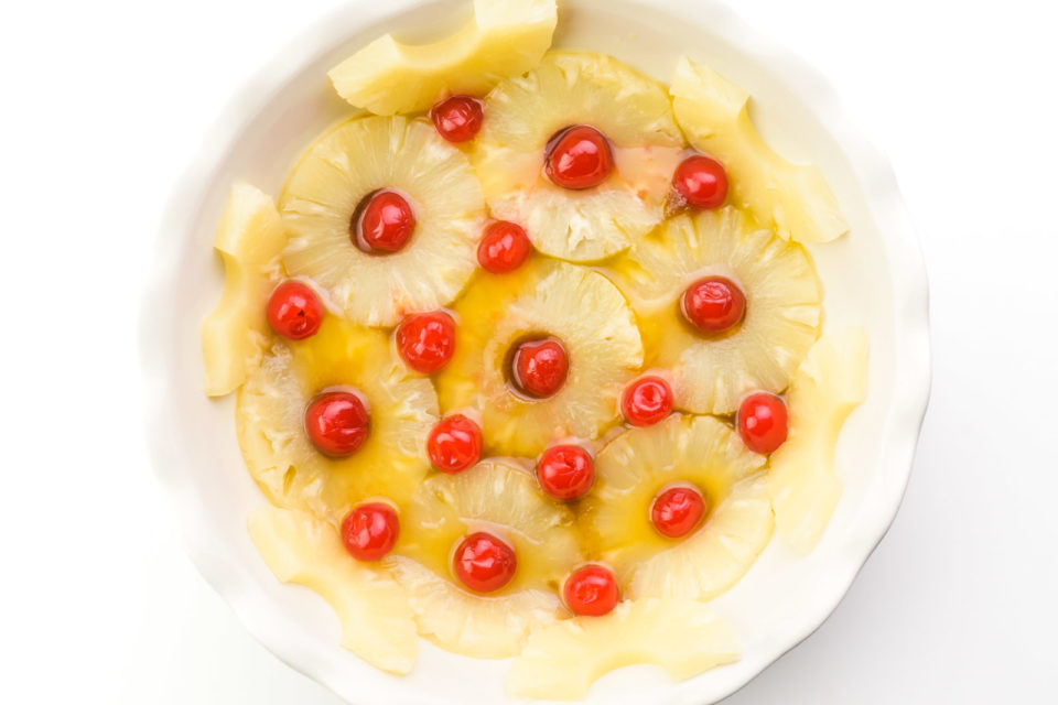 Looking down on a pie plate lined with pineapple rings with maraschino cherries inside.