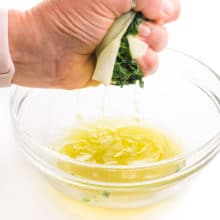A hand holds frozen spinach wrapped in a paper towel and is squeezing liquid from the spinach out into a bowl.
