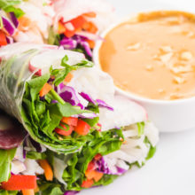 Vegan spring rolls are on a plate sitting next to peanut sauce.