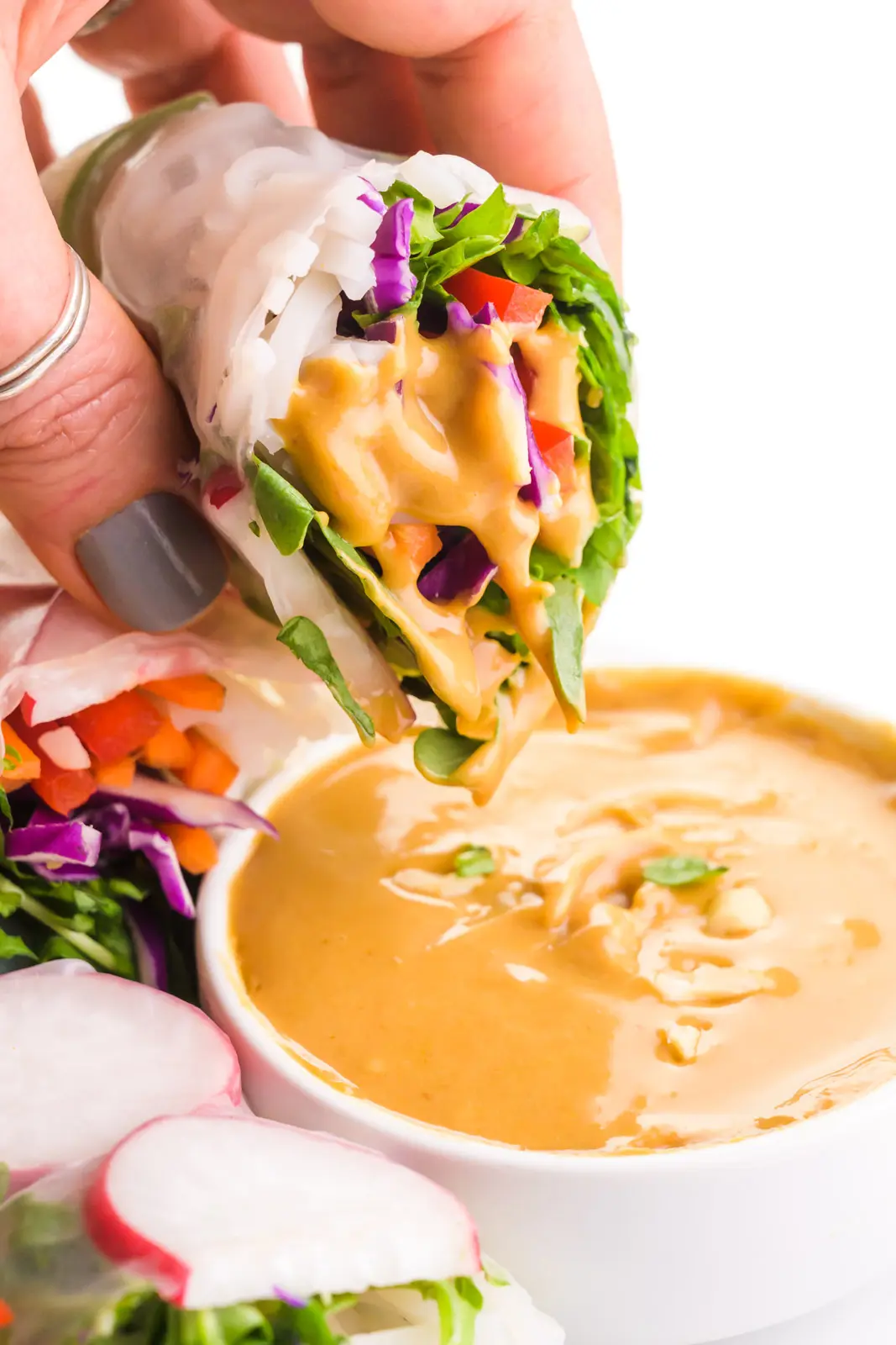 A hand holds a spring roll recently dipped in peanut sauce. There are more spring rolls around it.