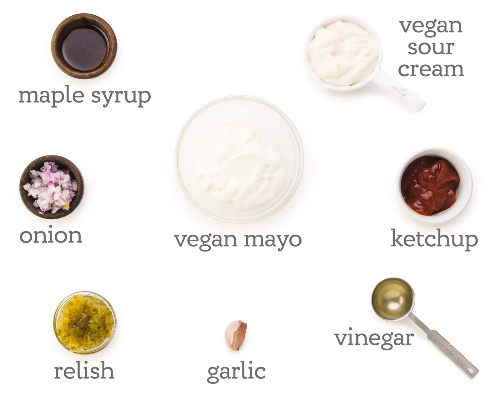 Ingredients are laid out on a white counter. The labels next to them read, vegan sour cream, ketchup, vinegar, garlic, relish, onion, maple syrup, and vegan mayo.