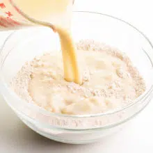 A milk mixture is being poured into a bowl with flour.