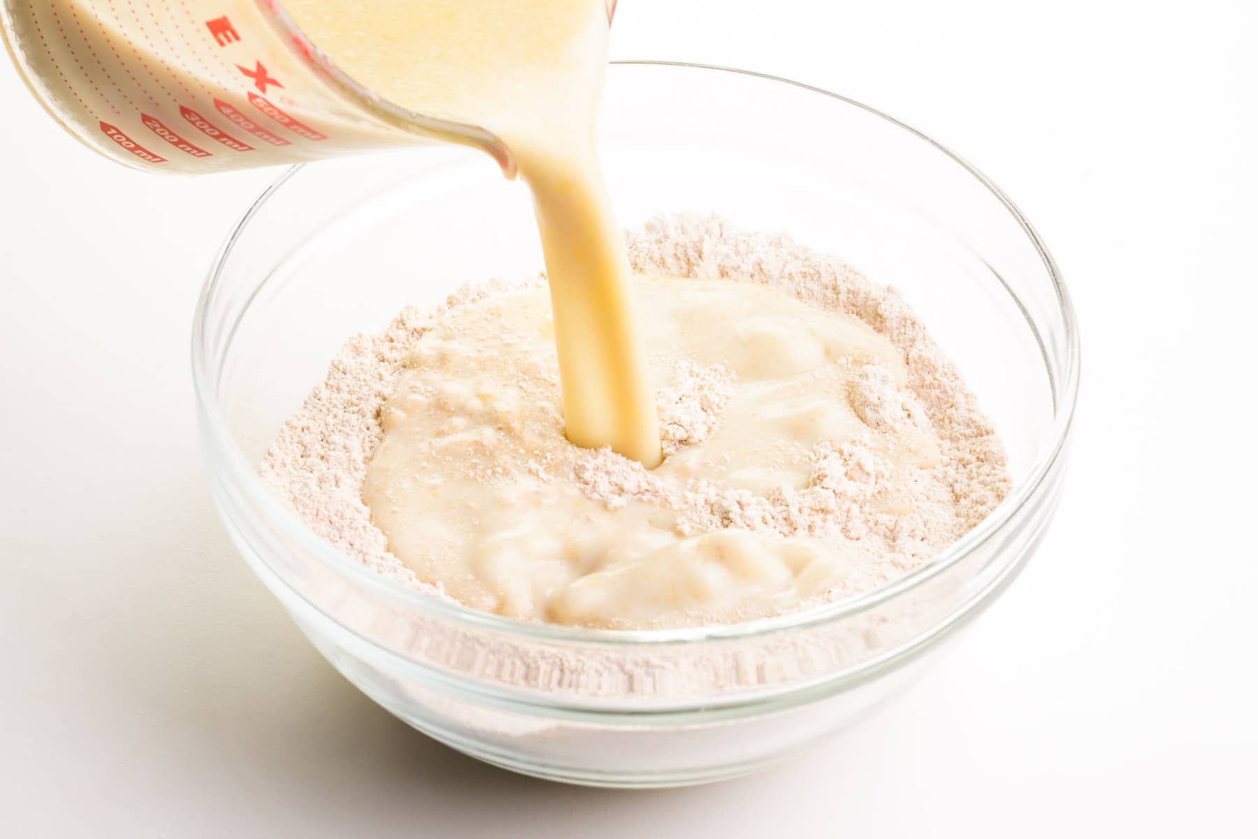 A milk mixture is being poured into a bowl with flour.