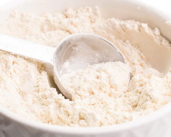 A measuring spoon sits in a bowl full of whole wheat pastry flour.