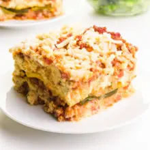 A serving of zucchini lasagna sits on a plate. There's another slice barely visible in the background.