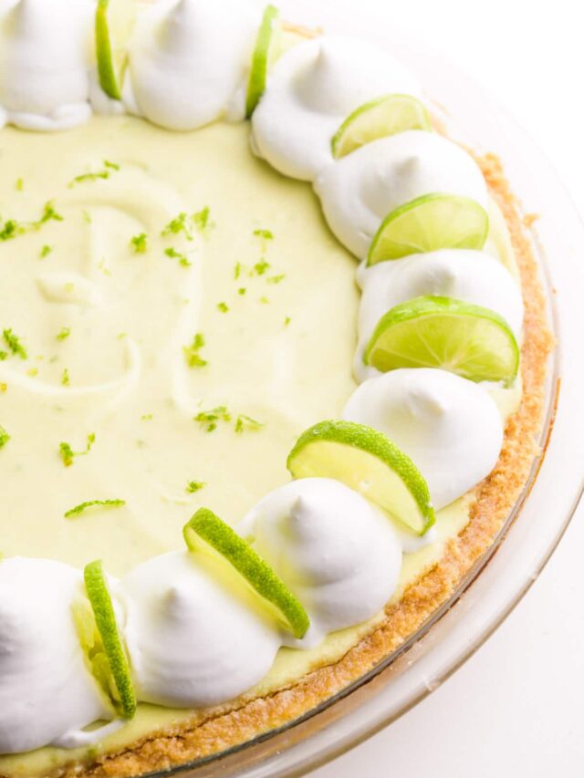 Looking down on a whole key lime pie with whipped cream dollops and lime slices around the edges.
