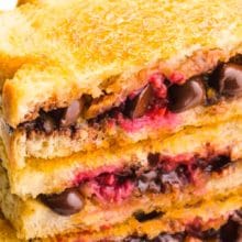 A stack of three chocolate grilled sandwiches shows melted chocolate and raspberries. There's a fresh raspberry in front of the stack. The text above it reads Pan Grilled Chocolate Sandwich.