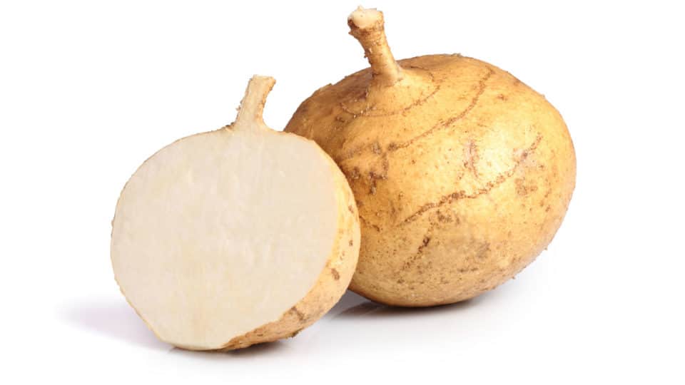 a jicama half sits next to a whole one on a white surface