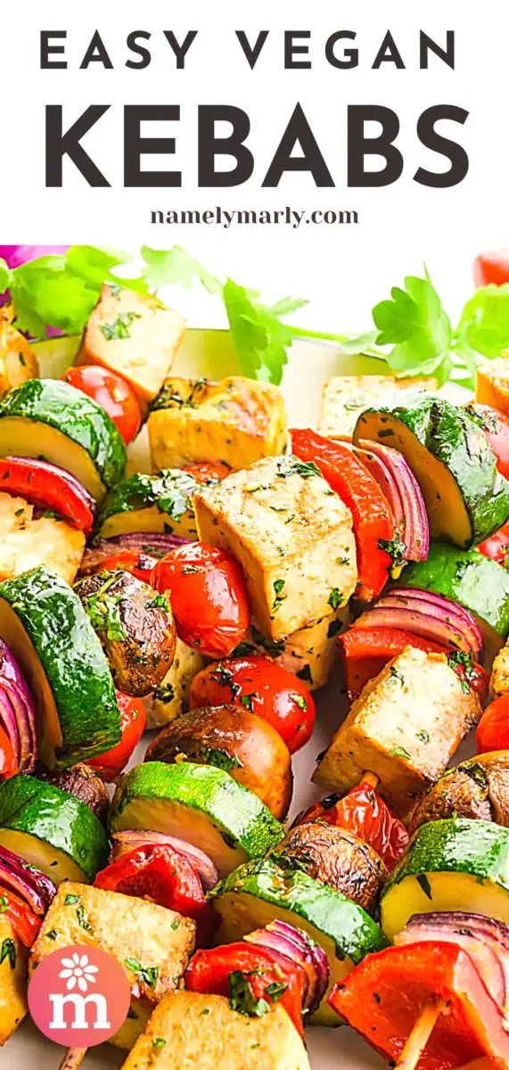 Several grilled skewers are full of veggies and tofu sitting on a plate. There are fresh herbs around the plate, cherry tomatoes, and red onions. The text at the top of the image reads, Vegan Kebabs.