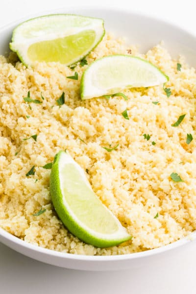 A bowl has riced cauliflower in it and there are lime wedges on top.