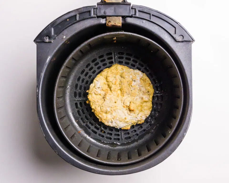A fried tofu patty is in an air fryer basket. 