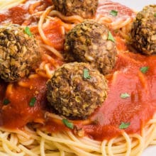 Vegan lentil meatballs sit atop spaghetti and red sauce on a white plate.