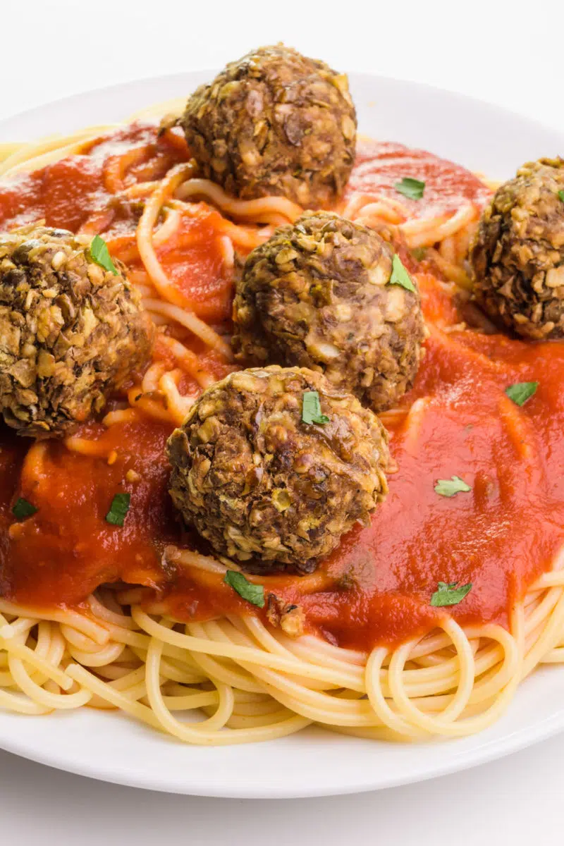 Vegan lentil meatballs sit atop spaghetti and red sauce on a white plate.