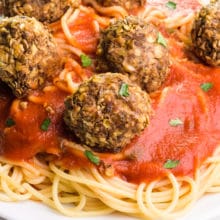 Lentil meatballs sit on top of red sauce and spaghetti on a plate.