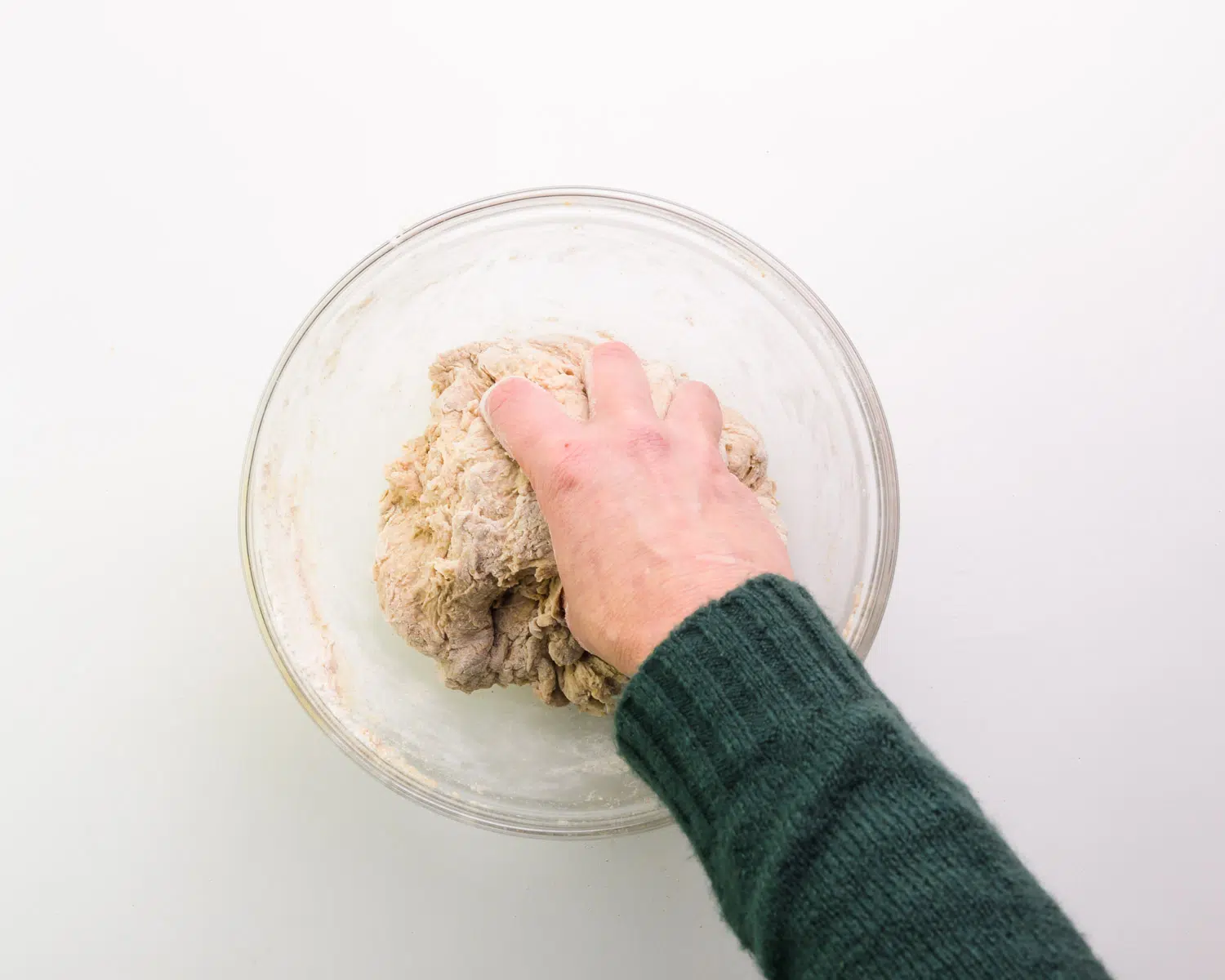 A hand is grabbing a ball of dough in a glass bowl.