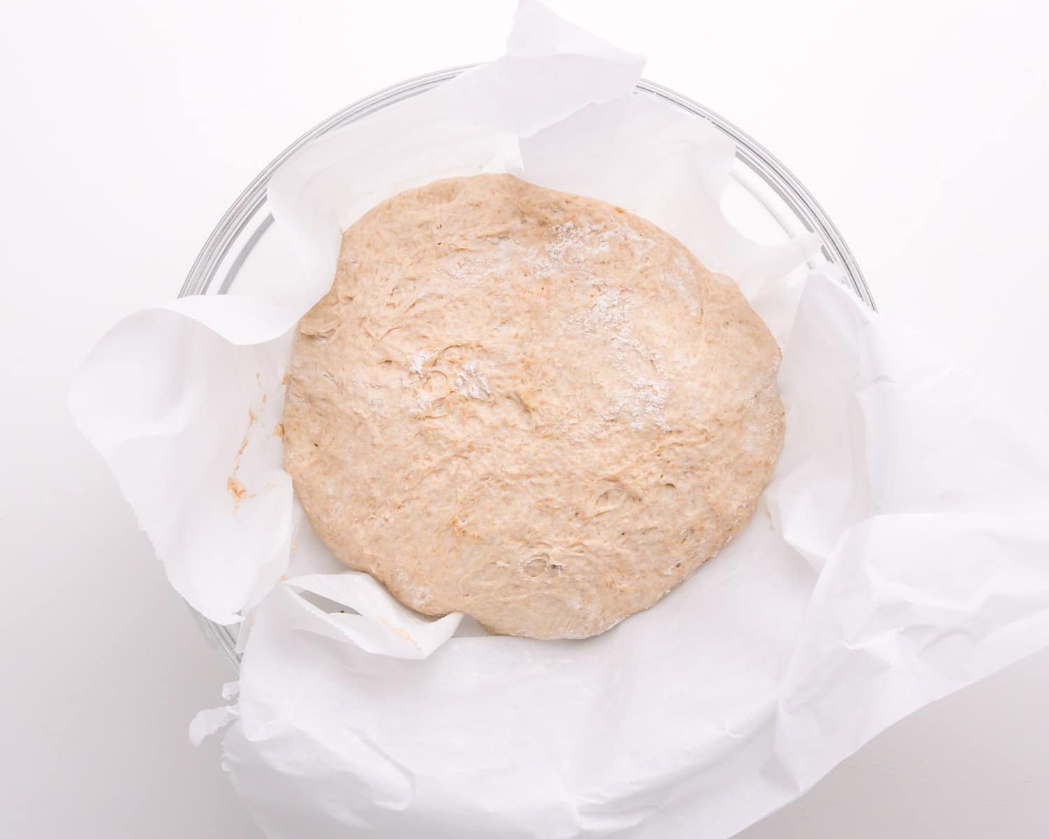 Dough sits on parchment paper, resting in a glass bowl.
