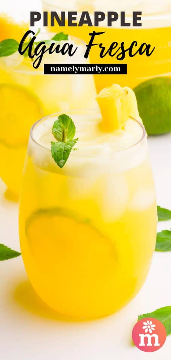 A glass of agua Fresca with mint and pineapple slices has another glass and a pitcher behind it.