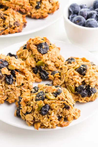 Vegan breakfast cookies sit on a plate with a plate of more cookies and a bowl of fresh blueberries in the background.