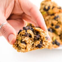 A hand holds a vegan breakfast cookie with a bite taken out.
