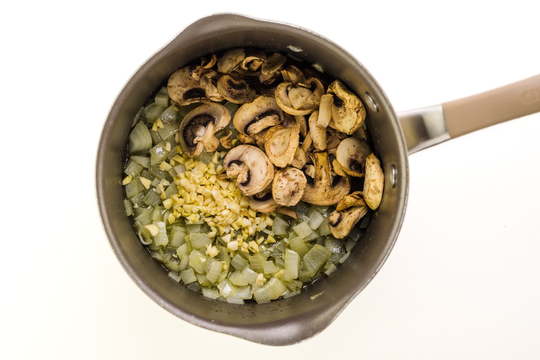 Mushrooms and chopped garlic are in a saucepan with cooked onions.