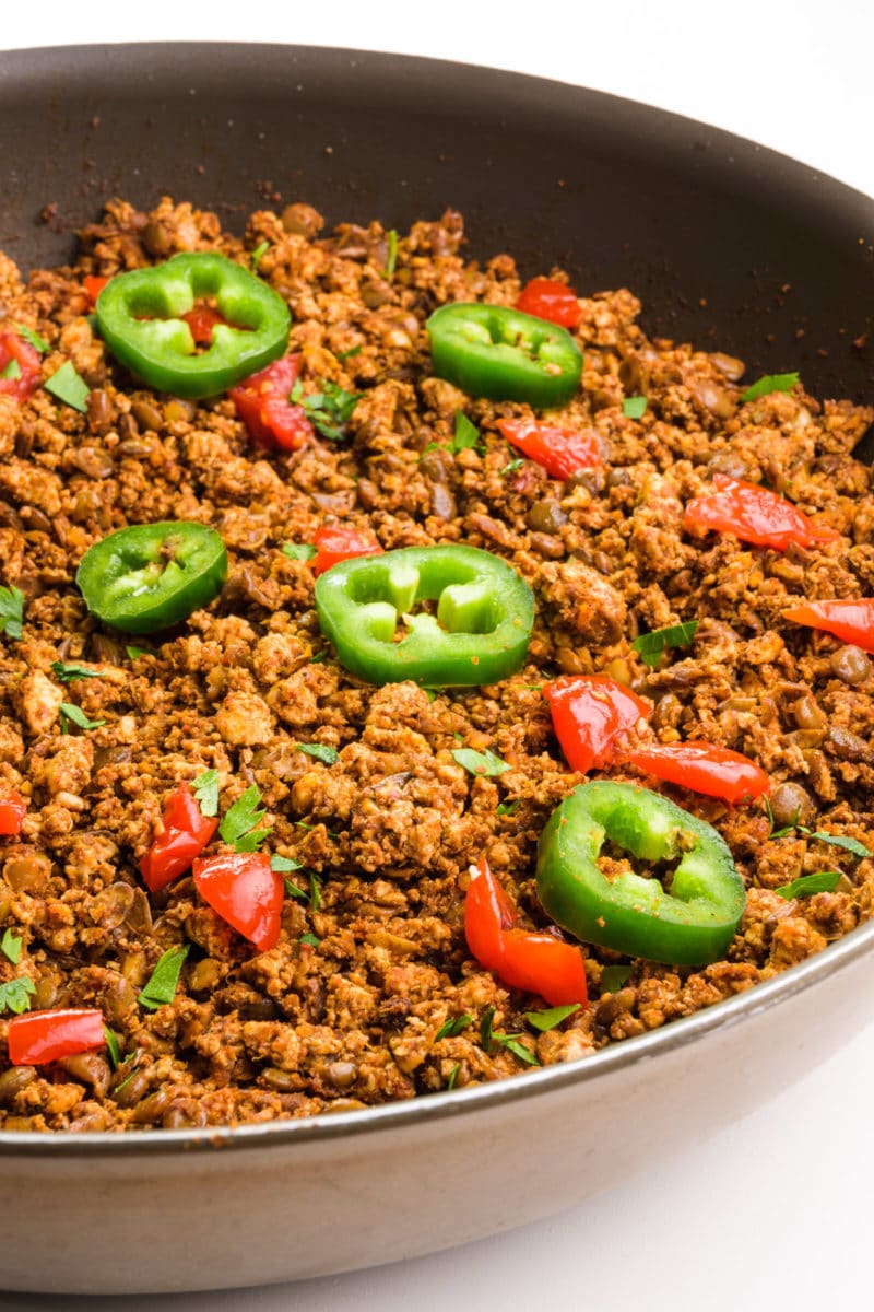 Looking into a skillet full of soy chorizo. It's topped with chopped tomatoes and sliced jalapeños.
