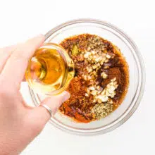 A hand holds a bowl of syrup, pouring it into a bowl with other sauce ingredients.