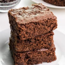 A stack of three brownies sits on a plate.