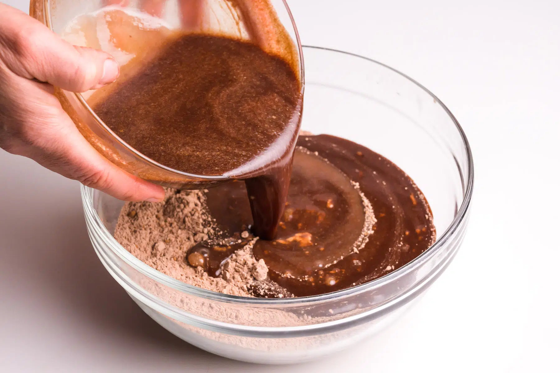 A liquid chocolate mixture is being poured into a bowl with a mixture of four and cocoa powder.