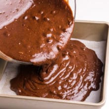 Brownie batter is being poured into a baking dish.